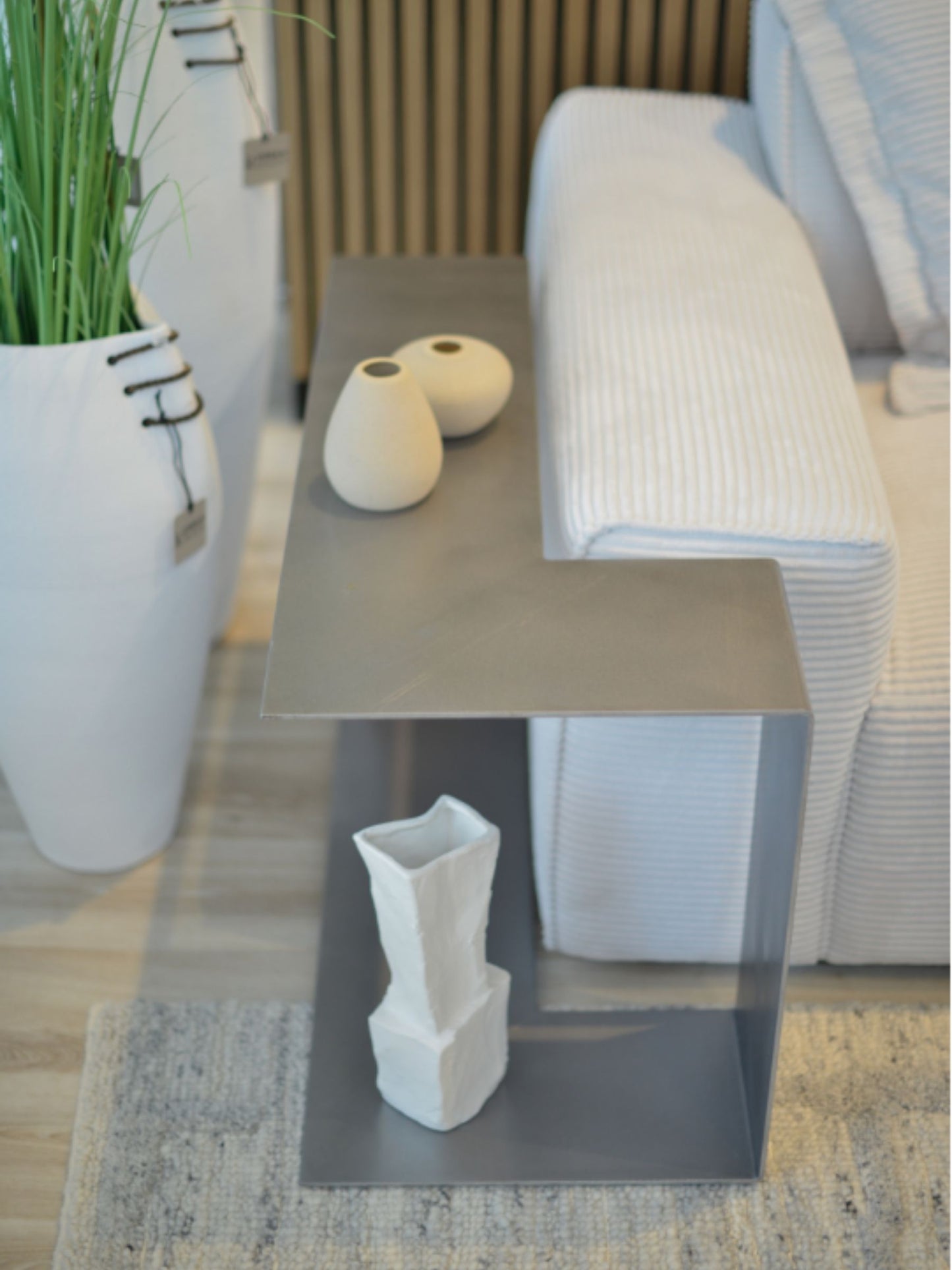 SIROKRIS Corner Sofa metal side table in steel next to a cream sofa.