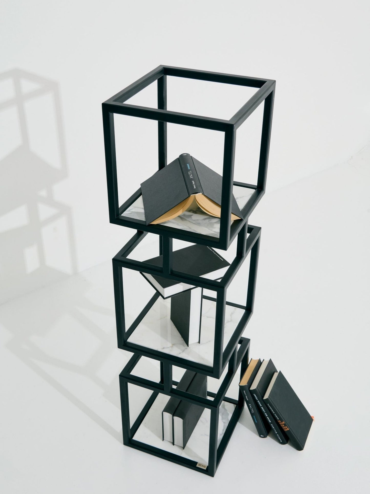 Modulares SIROKRIS Cube-Regal aus schwarzem Metall mit Marmorablagen, dekoriert mit Büchern auf weissem Hintergrund.